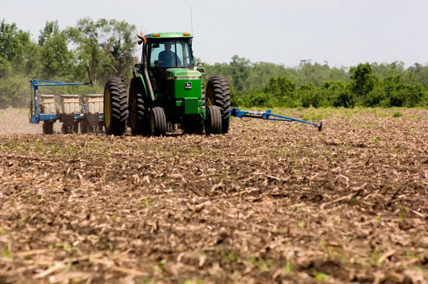 Farmer driving a tractor and planting equipment through a crop field.