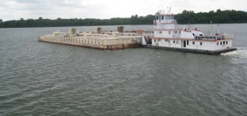 Tugboat pushing a cargo barge along a river.