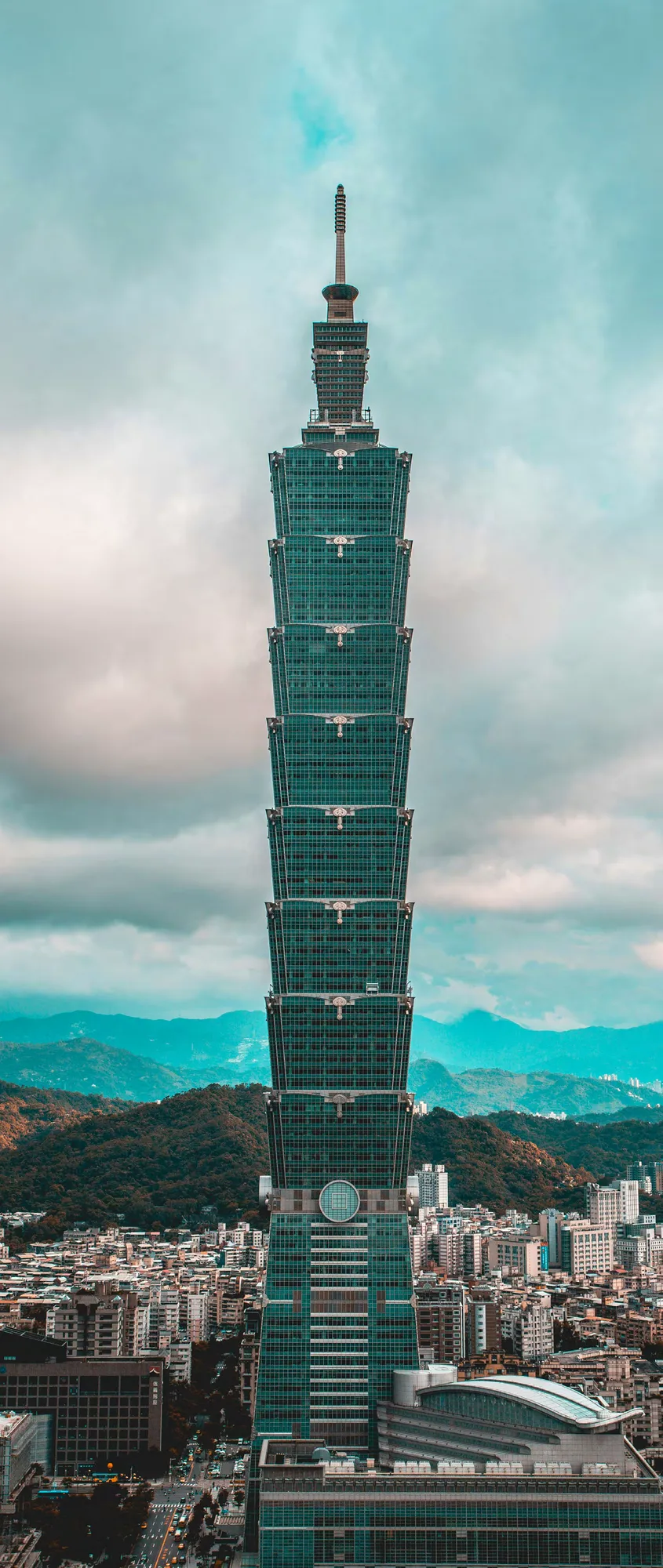 Taipei 101 skyscraper rising above the city skyline in Taipei, Taiwan, with mountains and clouds visible in the background.