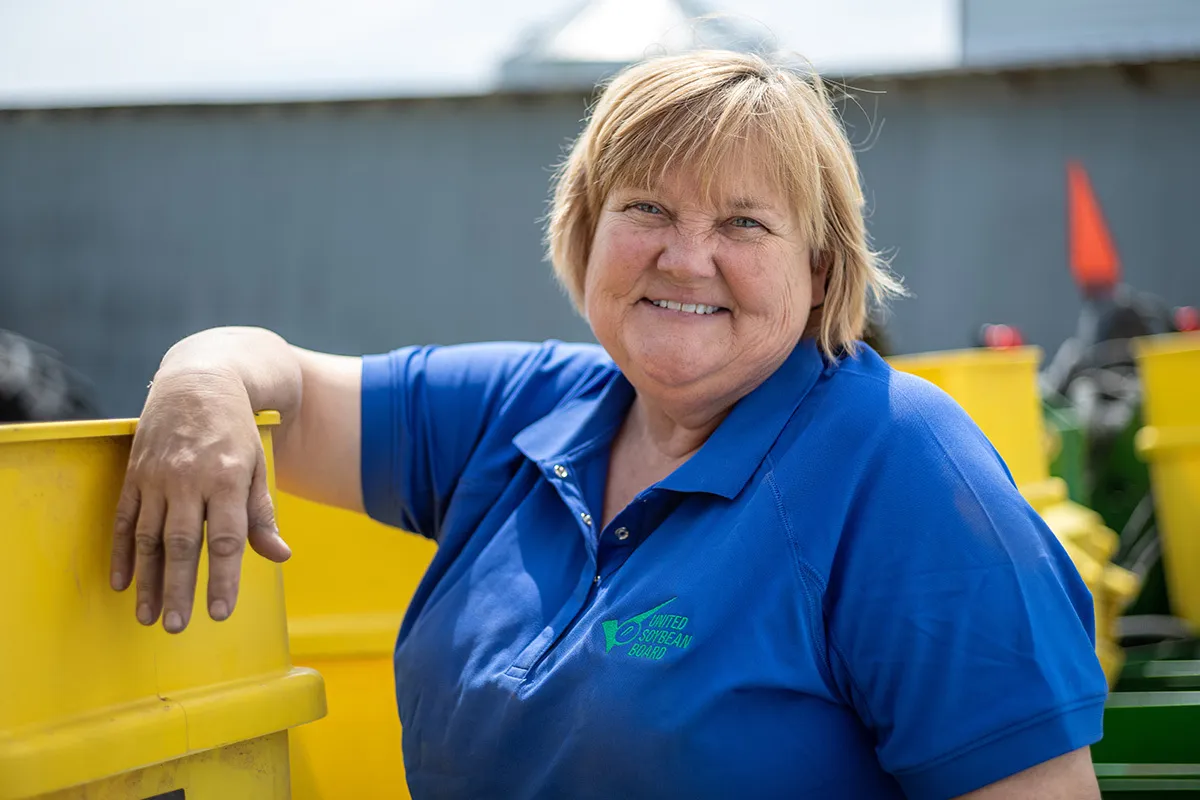 Woman wearing a United Soybean Board polo smiling beside farm equipment.