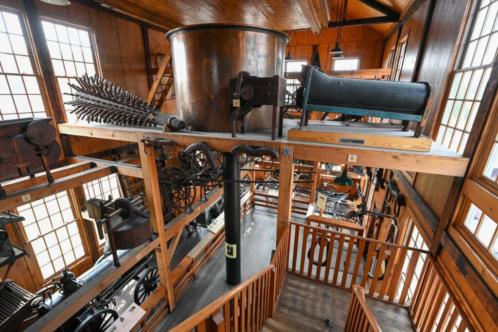 An interior view of a multi-level wooden museum filled with vintage agricultural machinery and equipment displays.