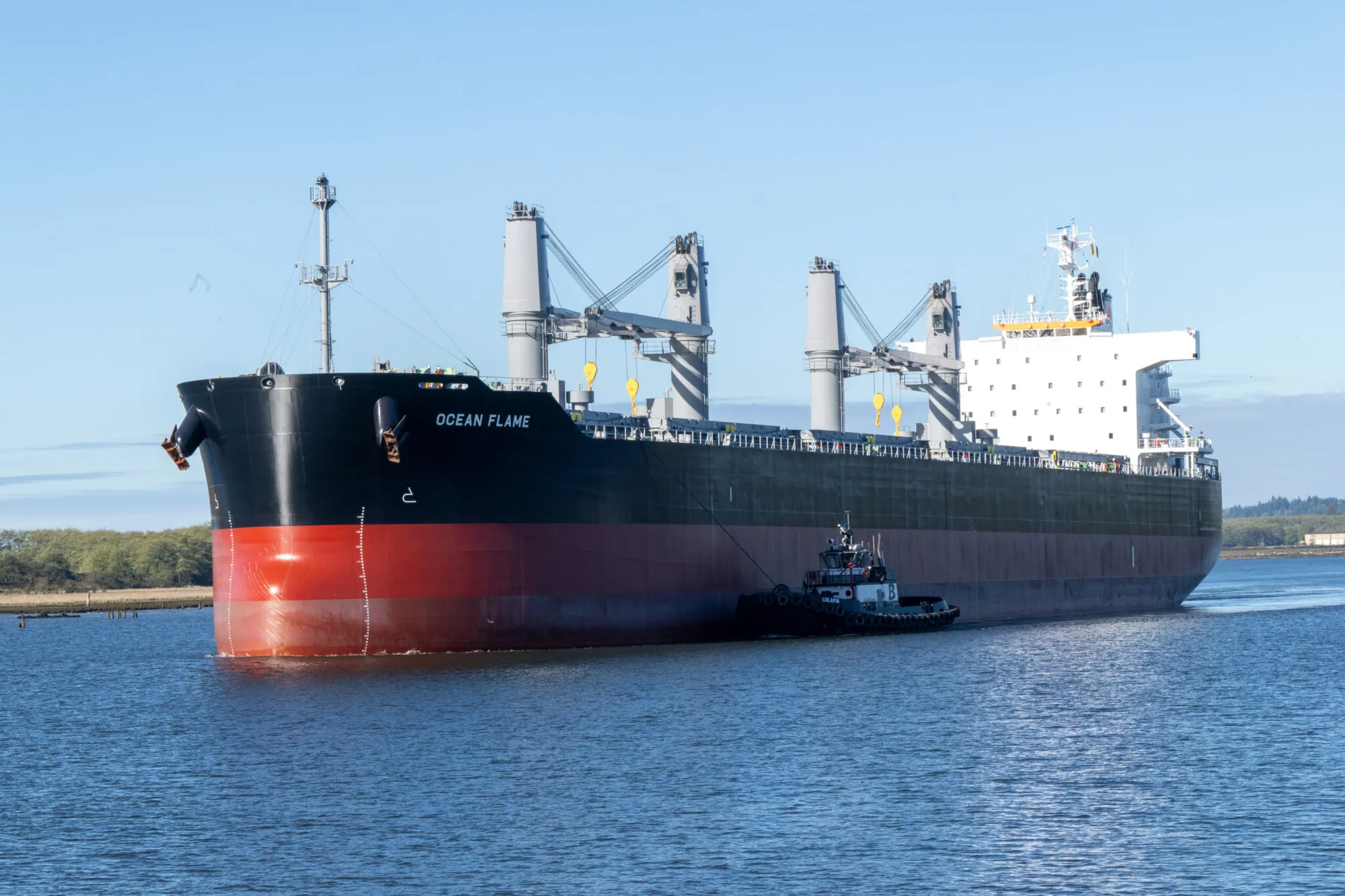 Large cargo ship traveling along a waterway with a tugboat alongside it.
