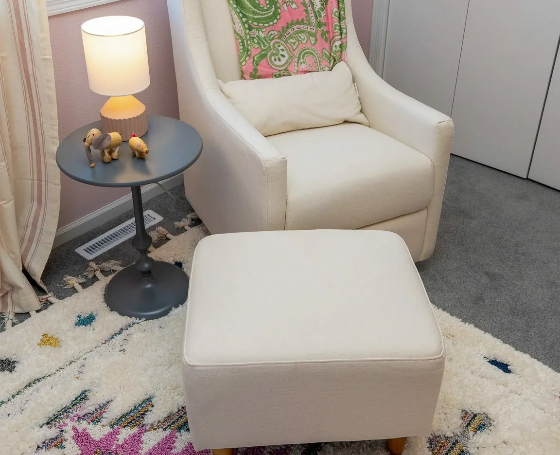 A cozy corner with a cream-colored armchair and matching ottoman beside a small round table holding a lamp and wooden toys.