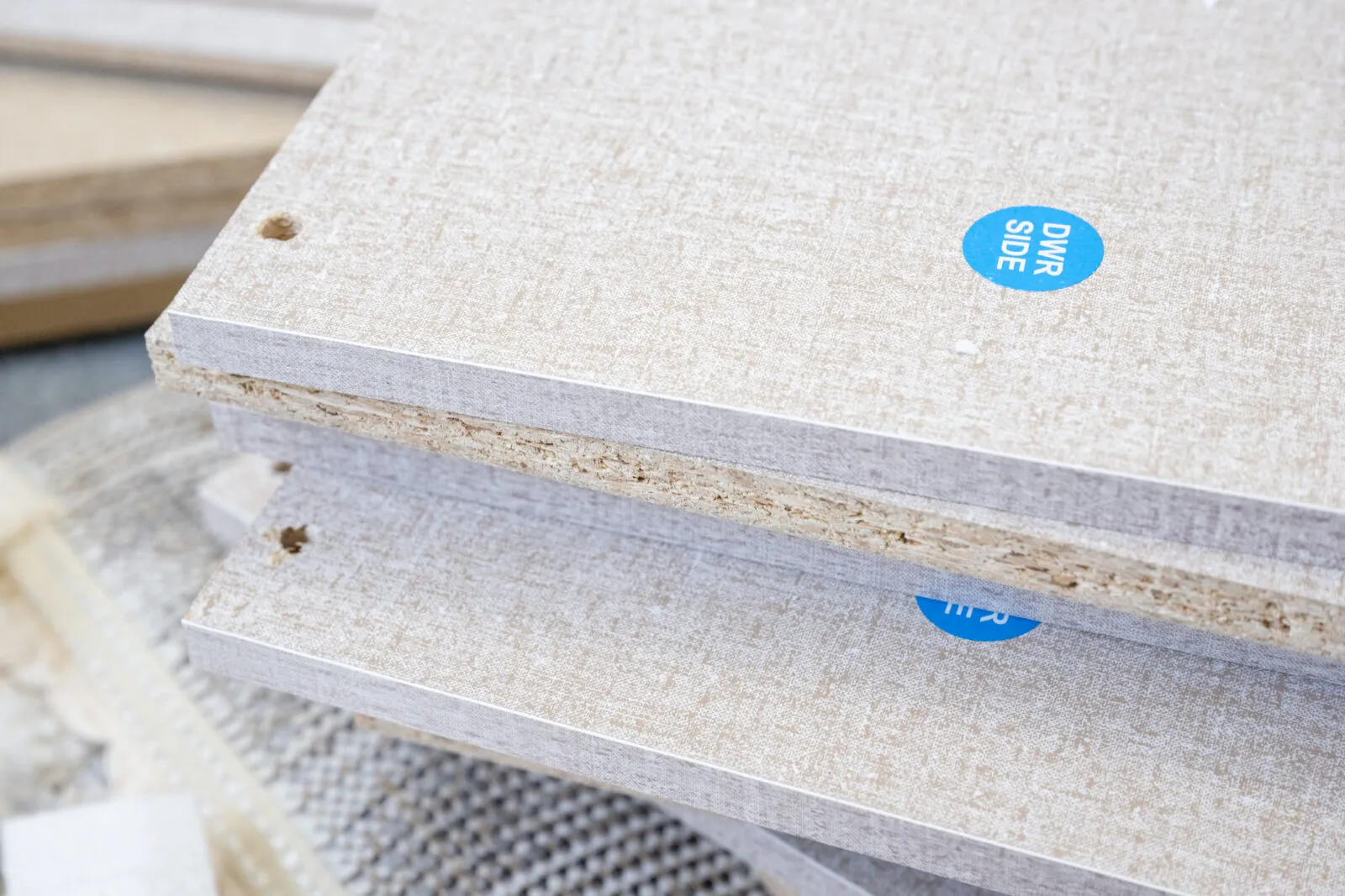 Close-up of stacked composite panels with a textured beige surface and a blue label reading ‘DWR SIDE.’