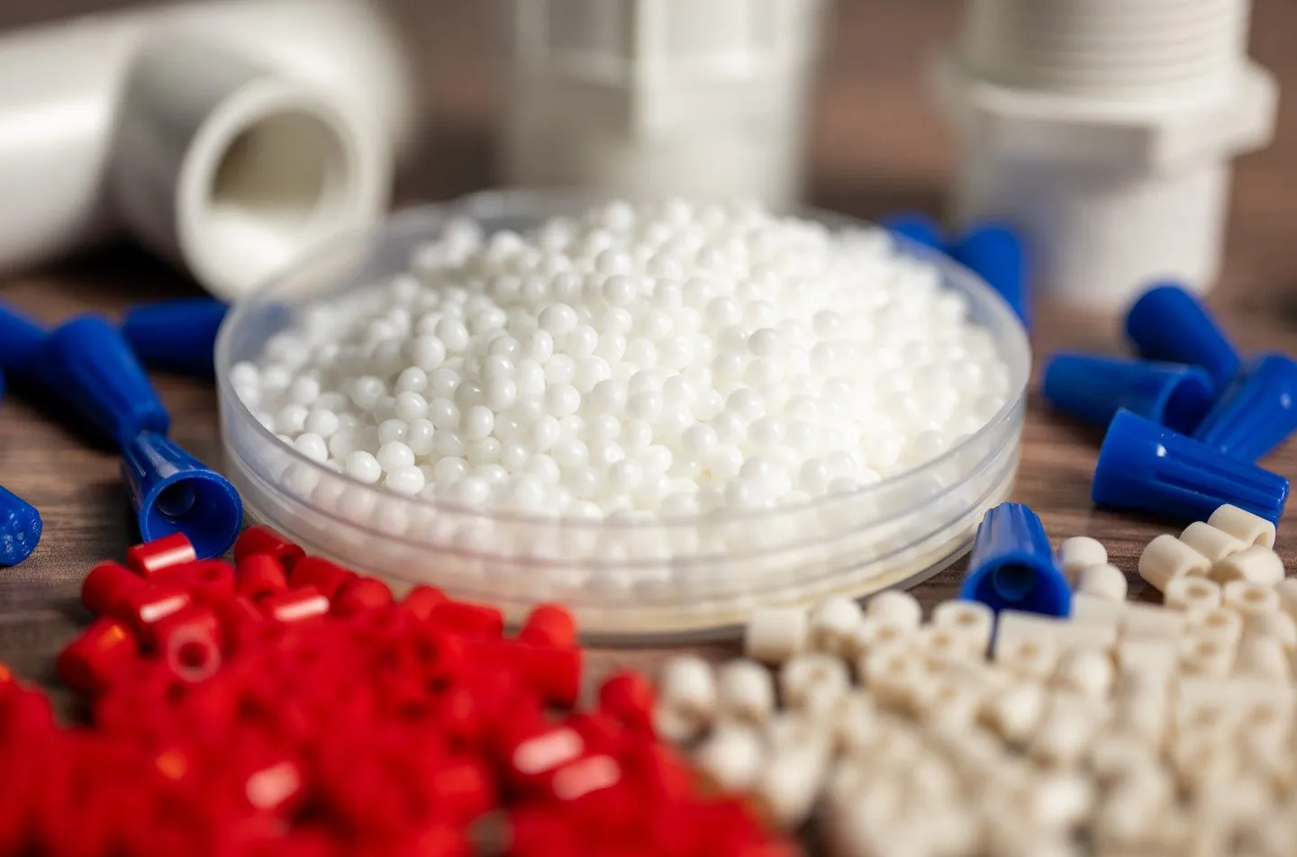 Close-up of white plastic pellets in a dish surrounded by various colored plastic components and connectors.