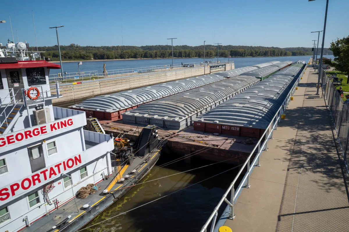 Covered barges and a towboat docked along the Mississippi River.