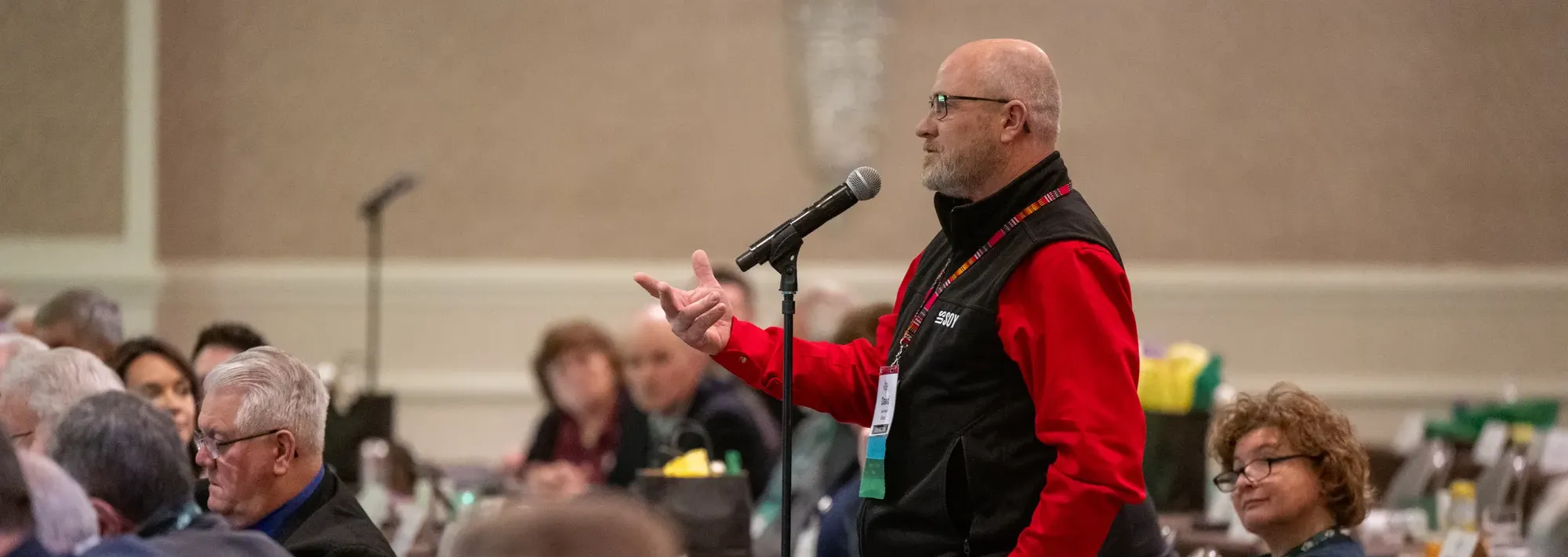 A farmer-leader speaking into a microphone during a United Soybean Board meeting while other board members listen.