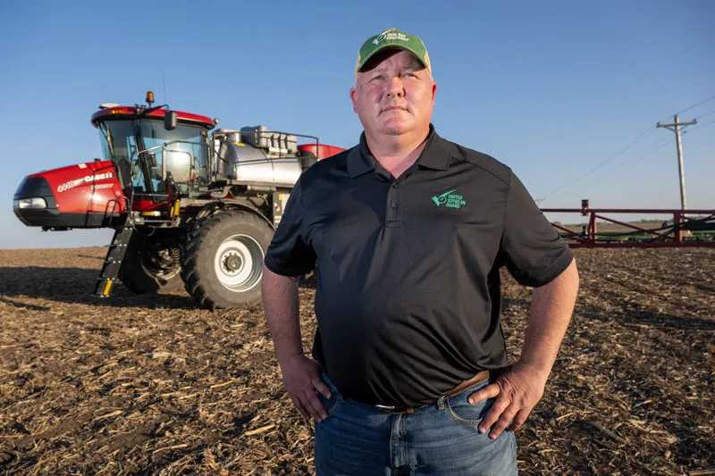 Farmer standing with his hands on his hips in front of a tractor in a field.