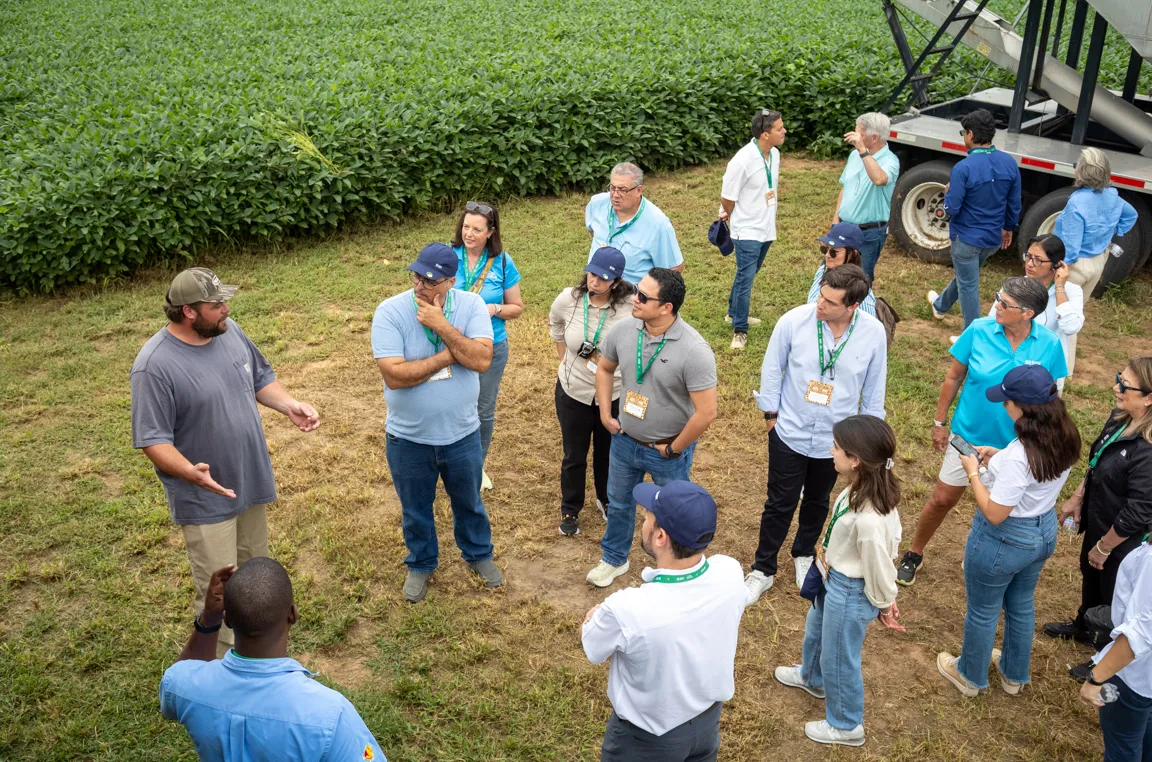 A group listens to a speaker outdoors near a field.