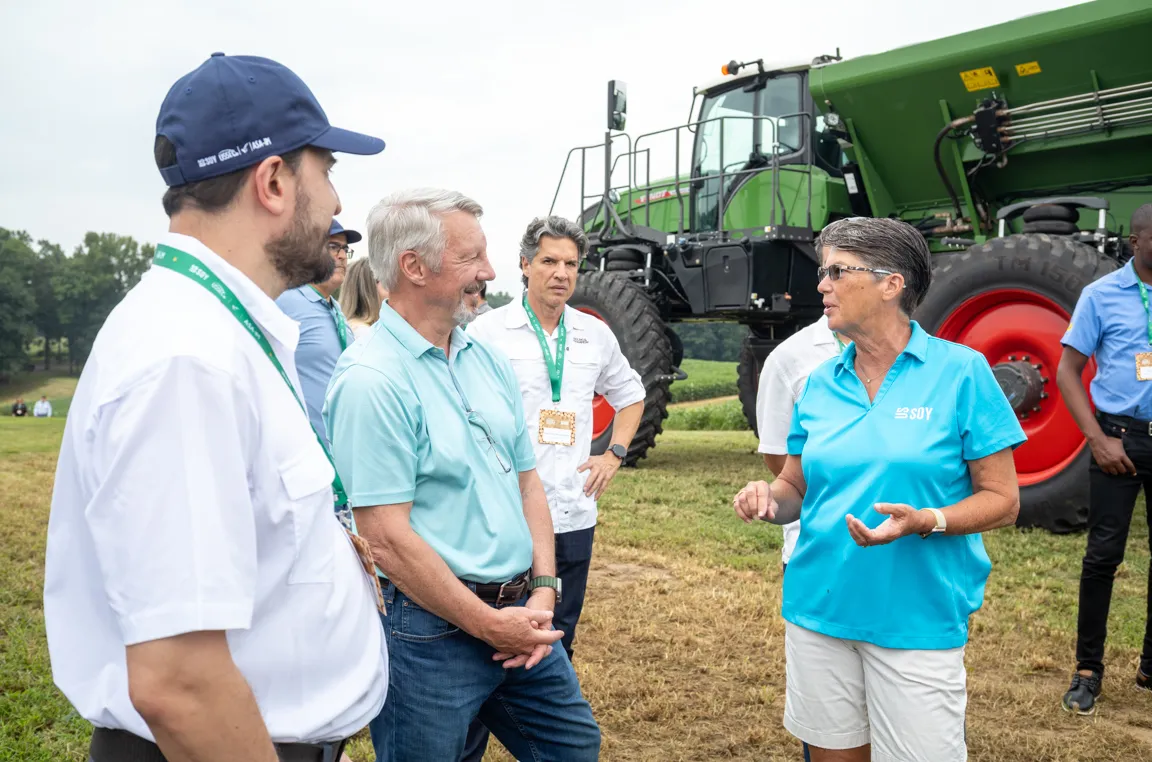 People talk beside large farm equipment outdoors.