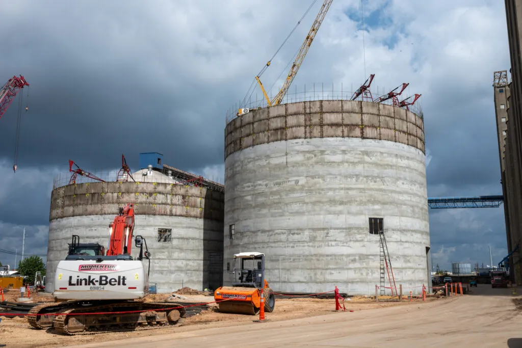 Large concrete storage structures under construction with cranes and heavy equipment.