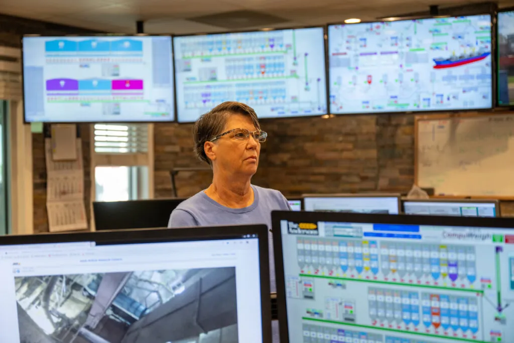 Worker in an industrial control room surrounded by monitoring screens.