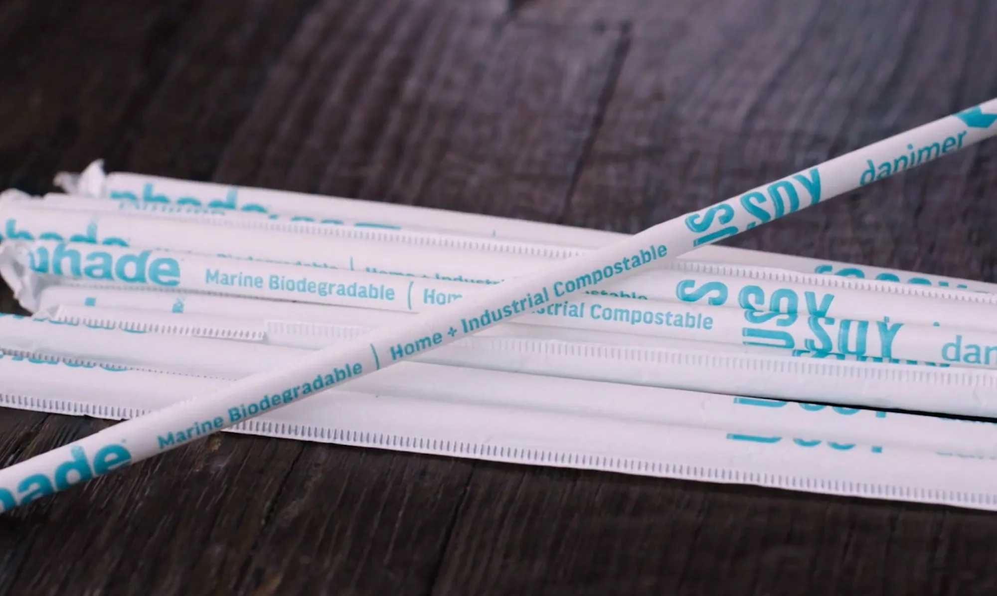 Close-up of compostable drinking straws made from soy-based materials, labeled with the U.S. Soy logo and sustainability certifications on the wrappers.