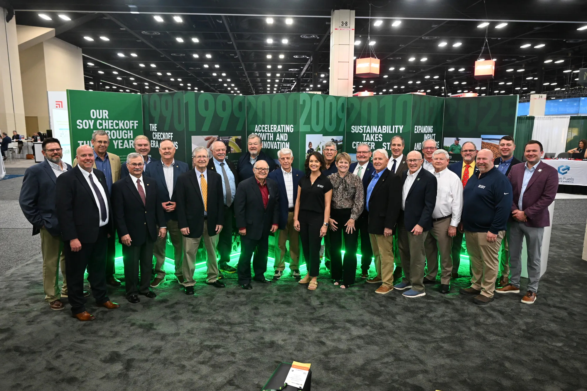 Soy Checkoff farmer-leaders posing at a trade show, standing in front of the 35th anniversary timeline.