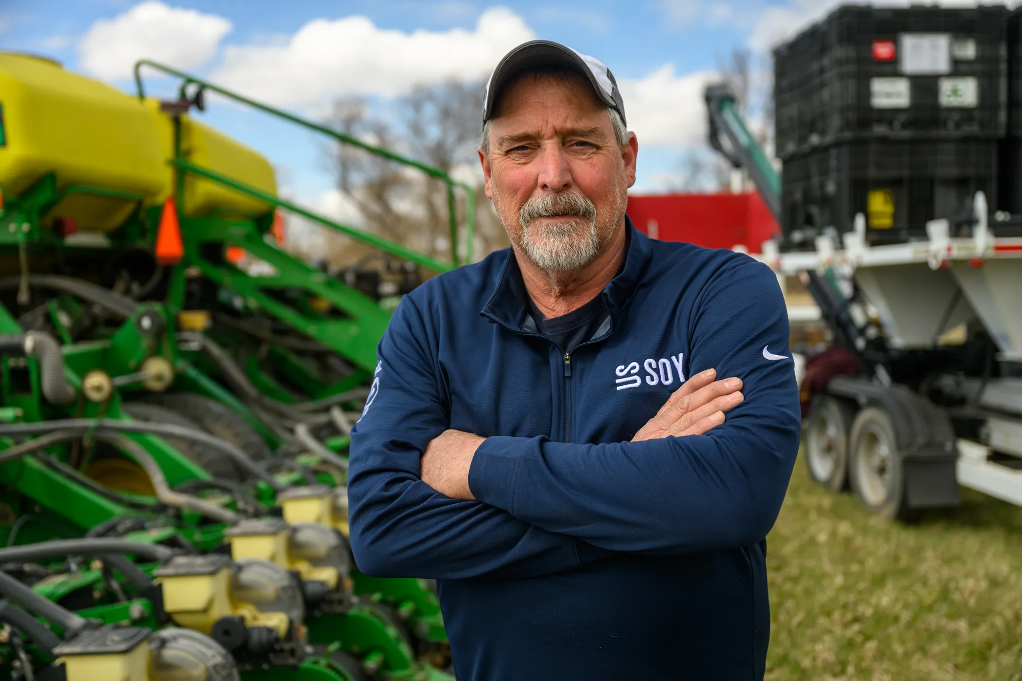 A farmer-leader stands in front of farming equipment with his arms crossed and a determined look on his face.