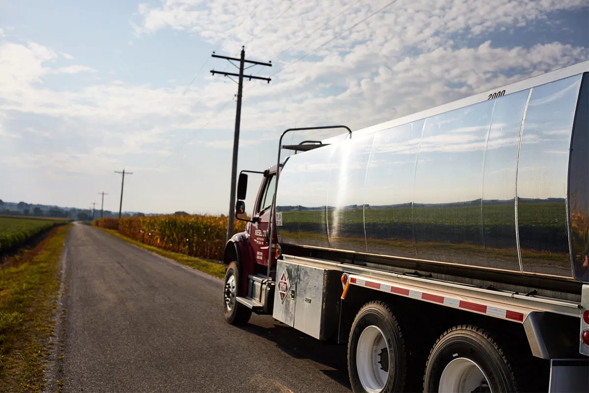 A biodiesel truck travels along a rural road beside soybean and corn fields.