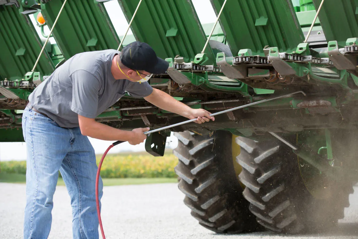 Farmer uses compressed air to clean debris from agricultural equipment.