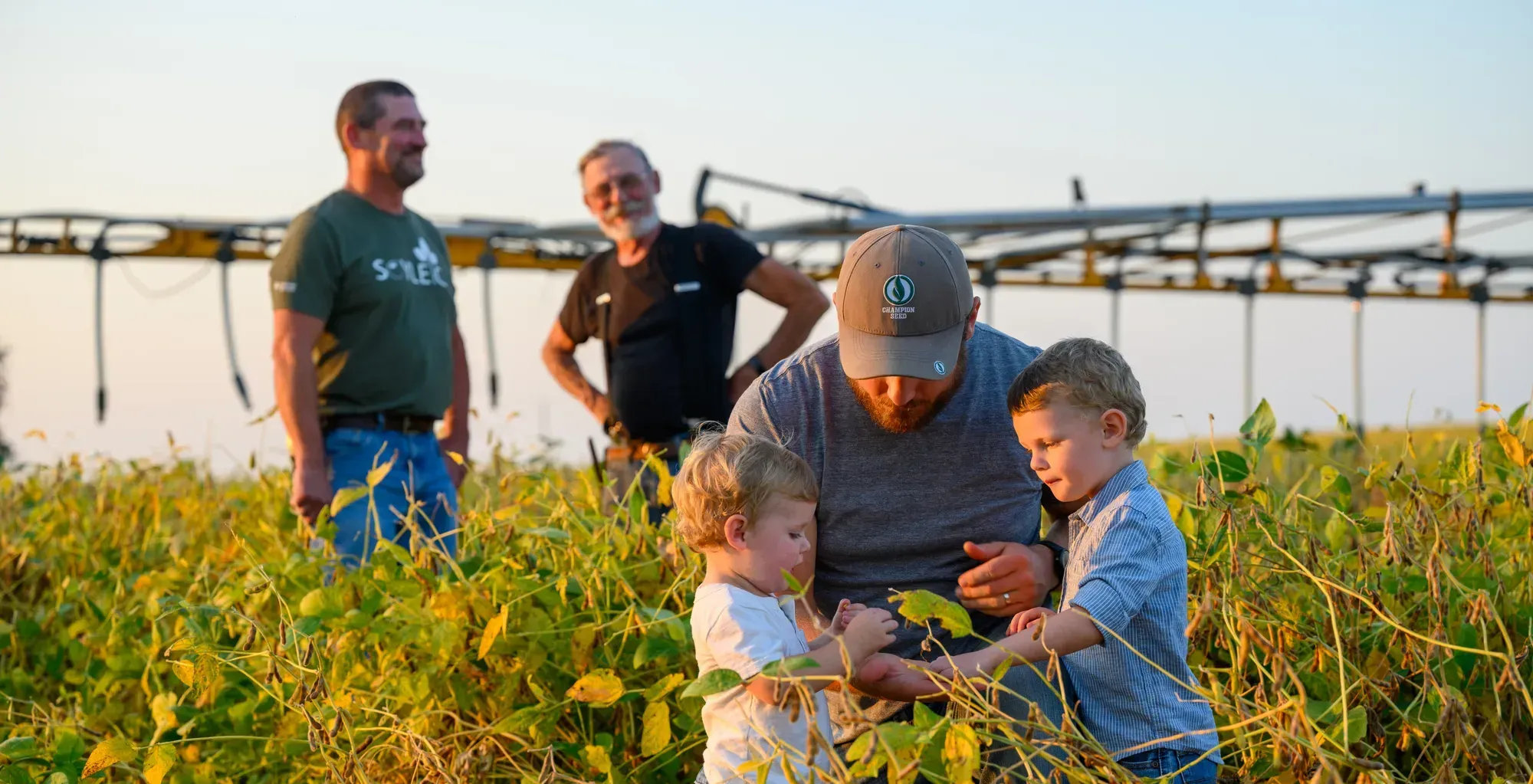 Multi-generational farm family standing in a soybean field, with a farmer showing soybean plants to two children.