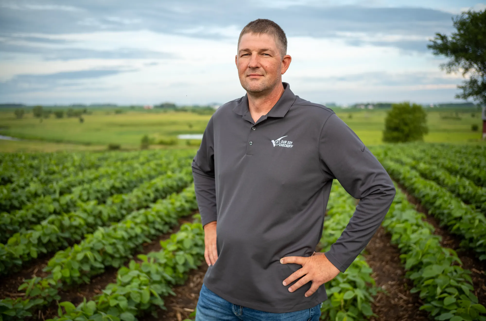 A soybean farmer standing in a field with rows of growing soybeans visible.