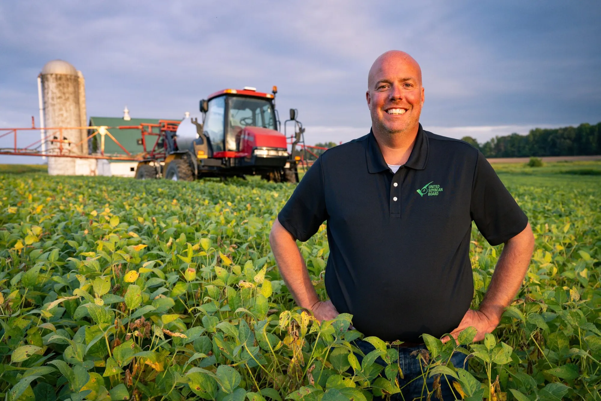 Brent Gatton stands in a soybean field with a tractor behind him.