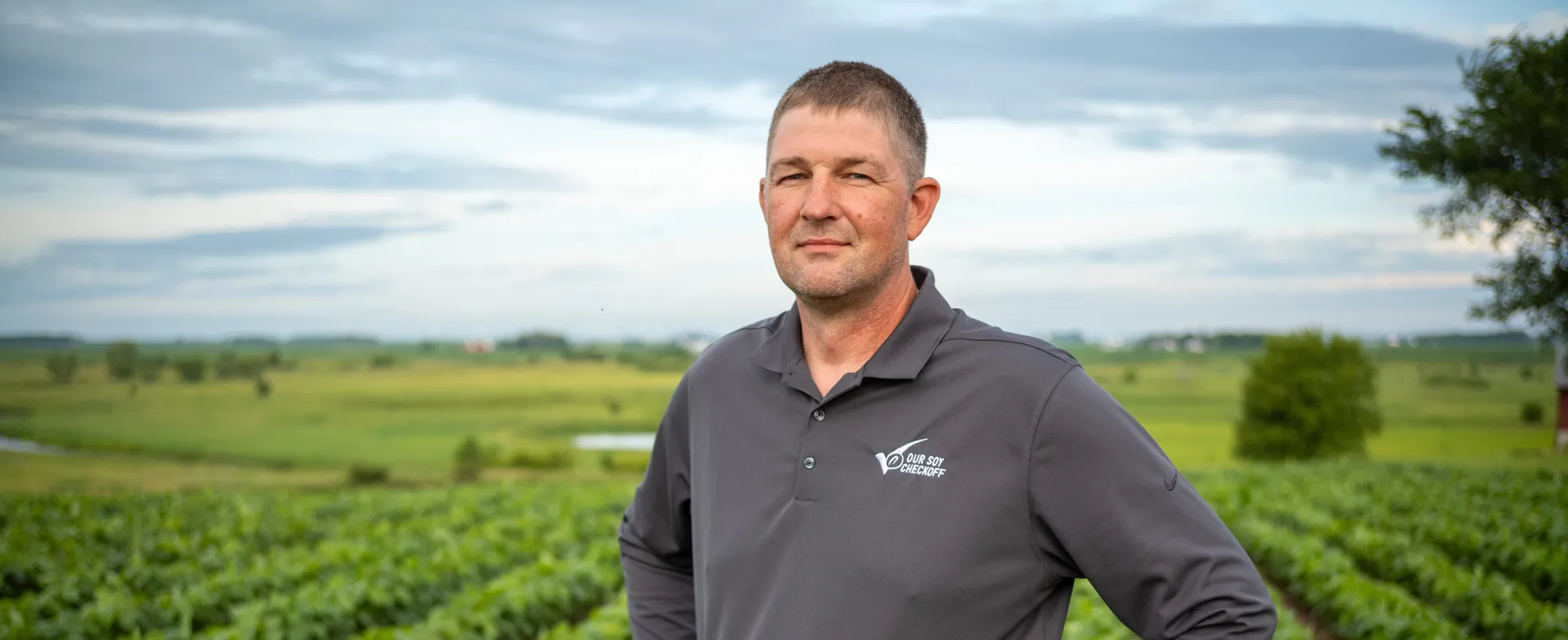 A soybean farmer standing in a field with rows of growing soybeans visible.