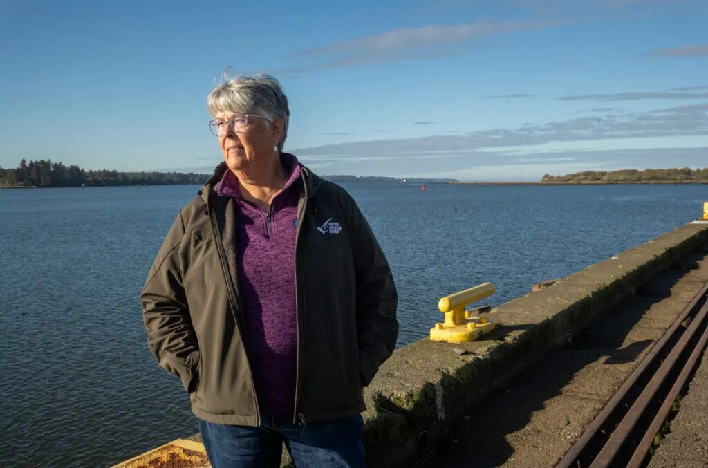 A woman standing on a waterfront pier, looking out over the water on a clear day.