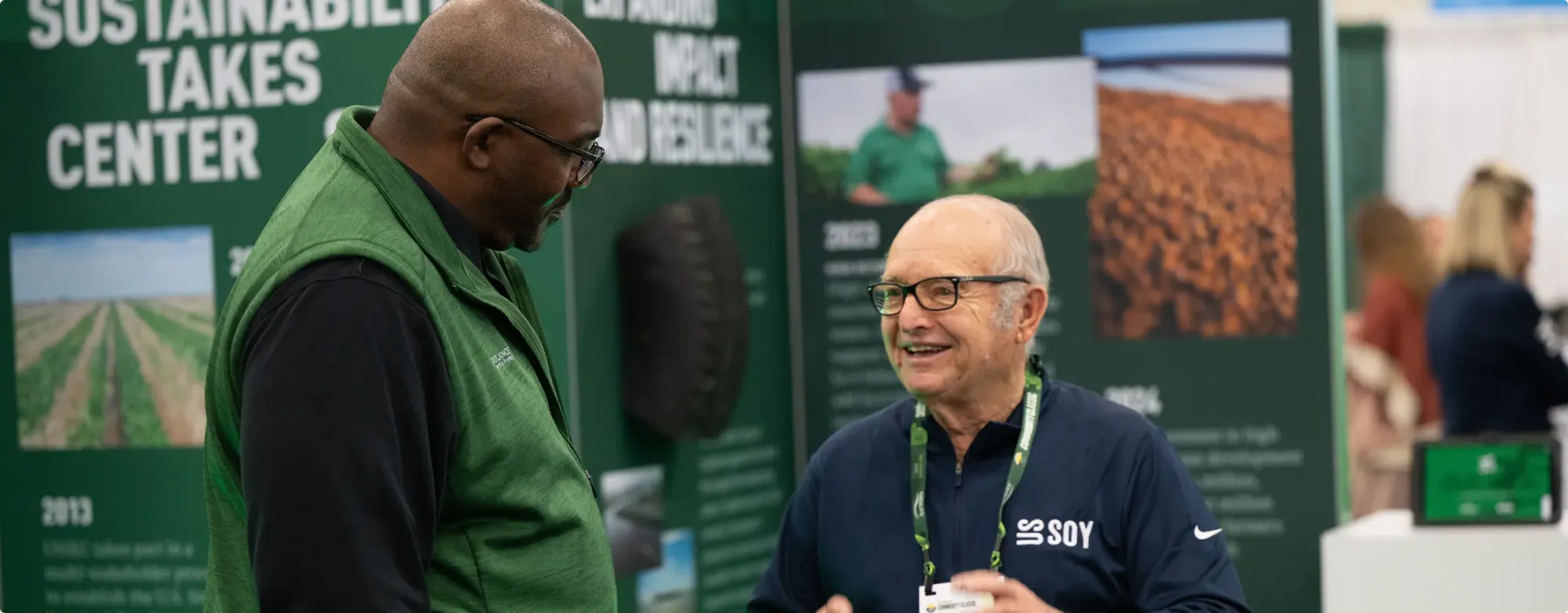 Two men talking at a soy industry exhibition booth.