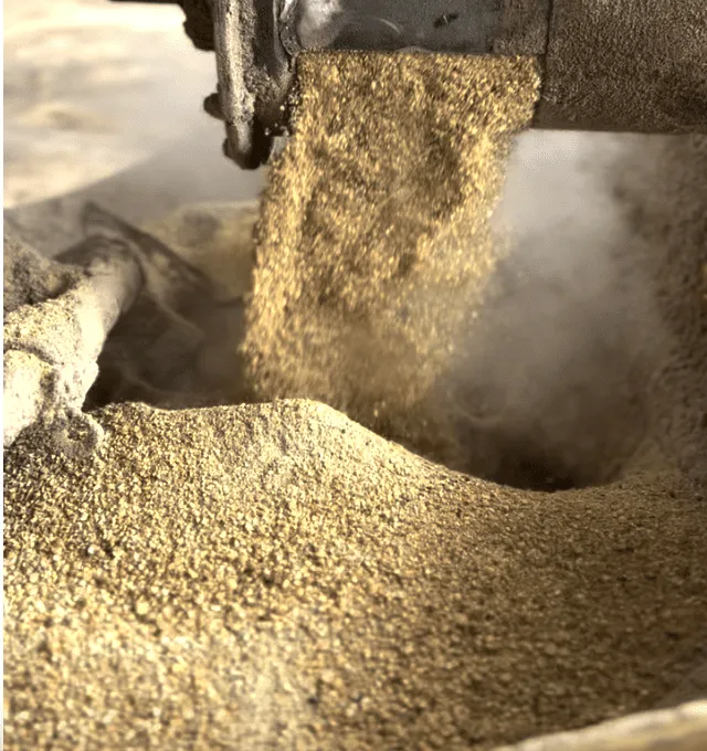 A stream of powdered feed or grain pouring from a chute into a growing pile.