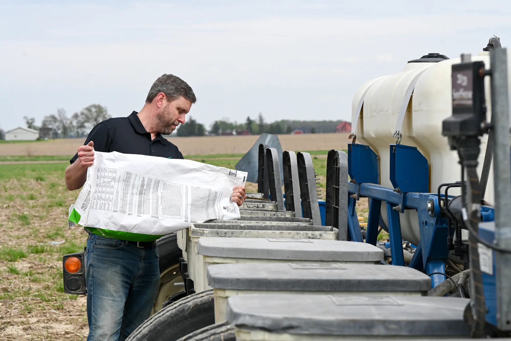 Farmer loading soybean seed into a planter in a field.