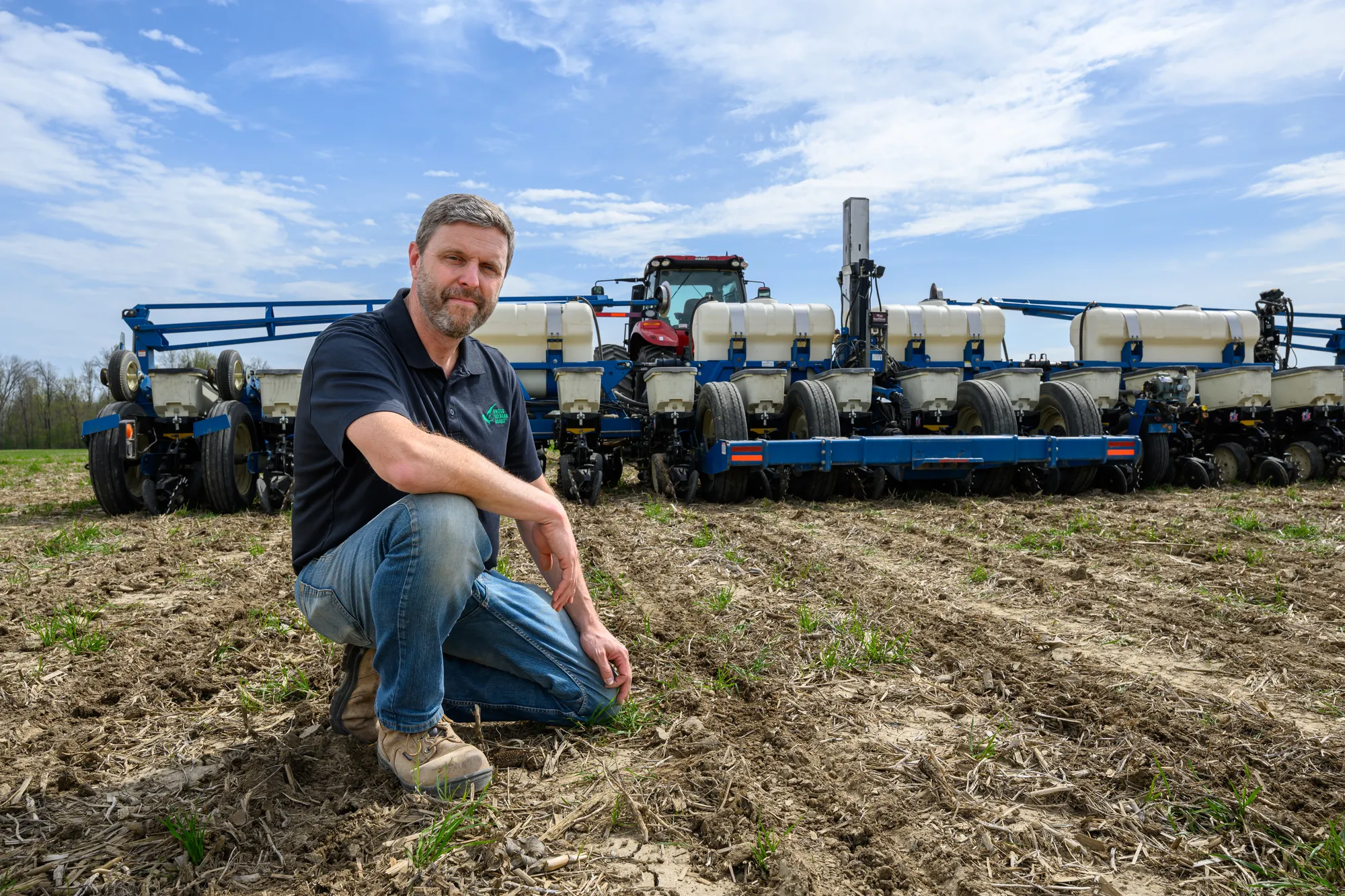 farmer knelling in field in front of equipment
