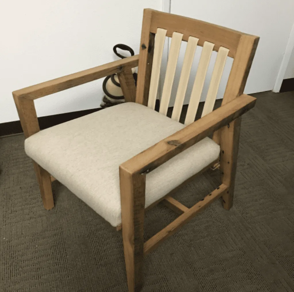 A wooden chair with a slatted back and a cushioned beige seat, featuring a simple, rustic design.