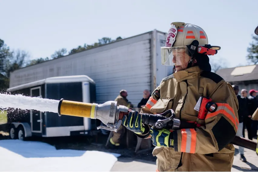 Firefighter sprays soy-based firefighting foam from a hose during a demonstration.