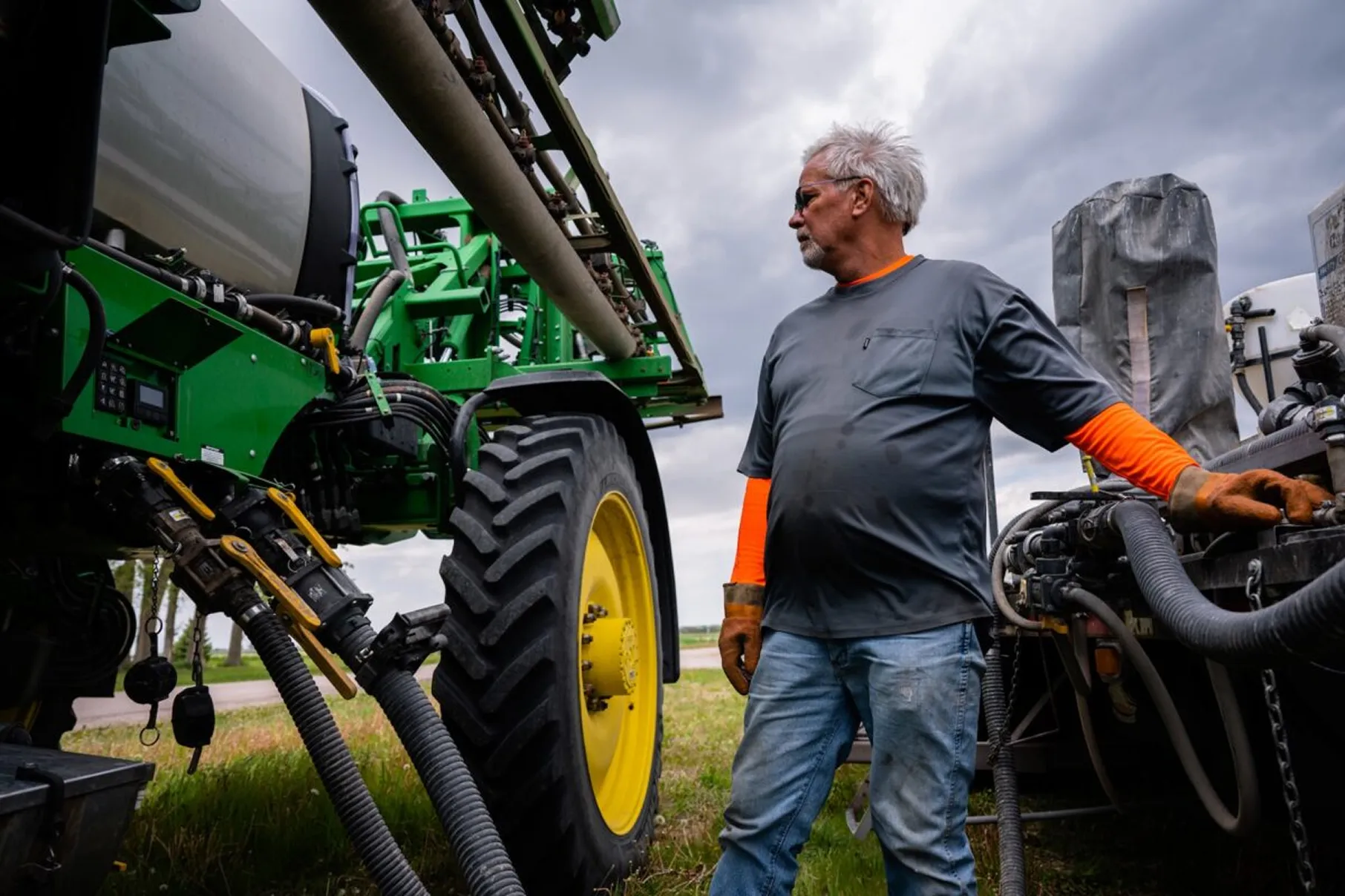 Farmer wearing protective gloves working beside a large agricultural sprayer.