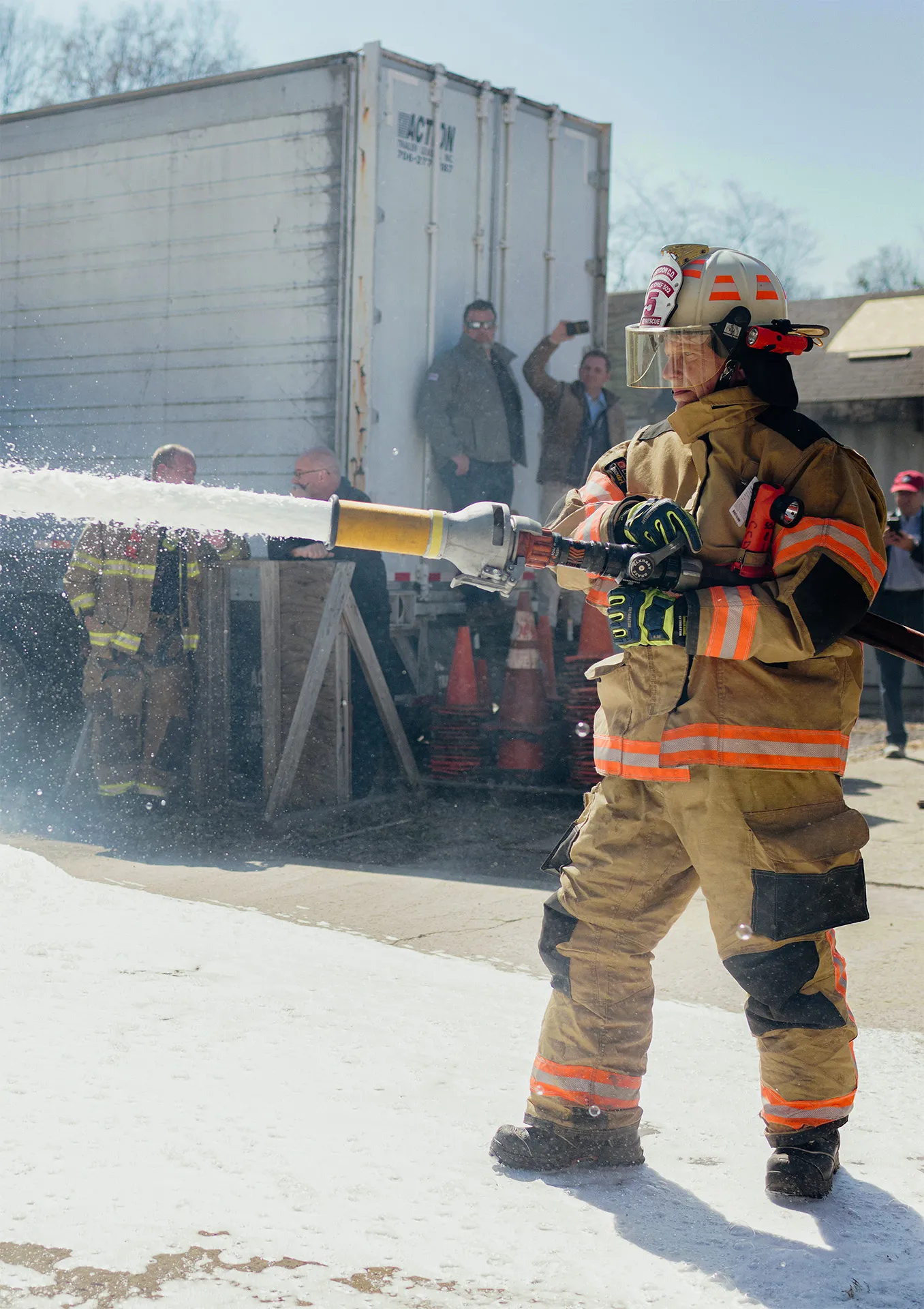 A firefighter in full protective gear sprays Firefighting SoyFoam™ from a high-pressure hose.