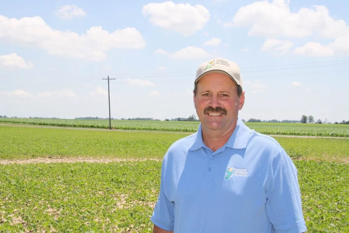 Soybean farmer wearing an Indiana Soybean Alliance shirt and cap stands in front of a green crop field.