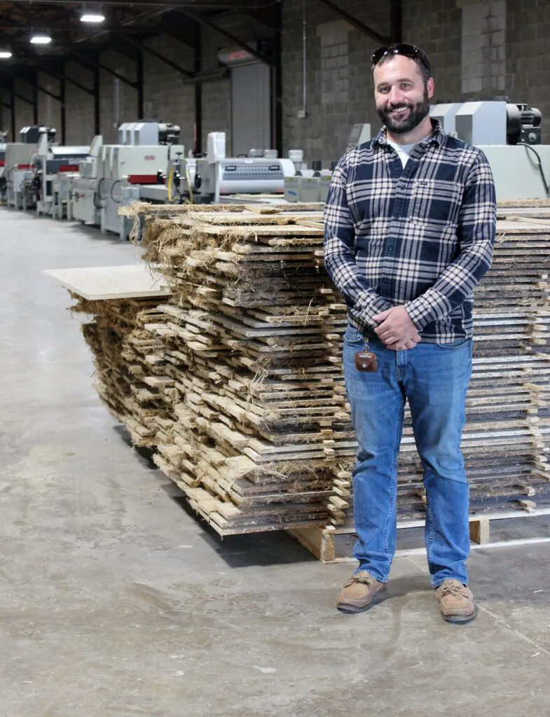 A man standing in a manufacturing facility beside stacked raw HempWood boards awaiting processing.