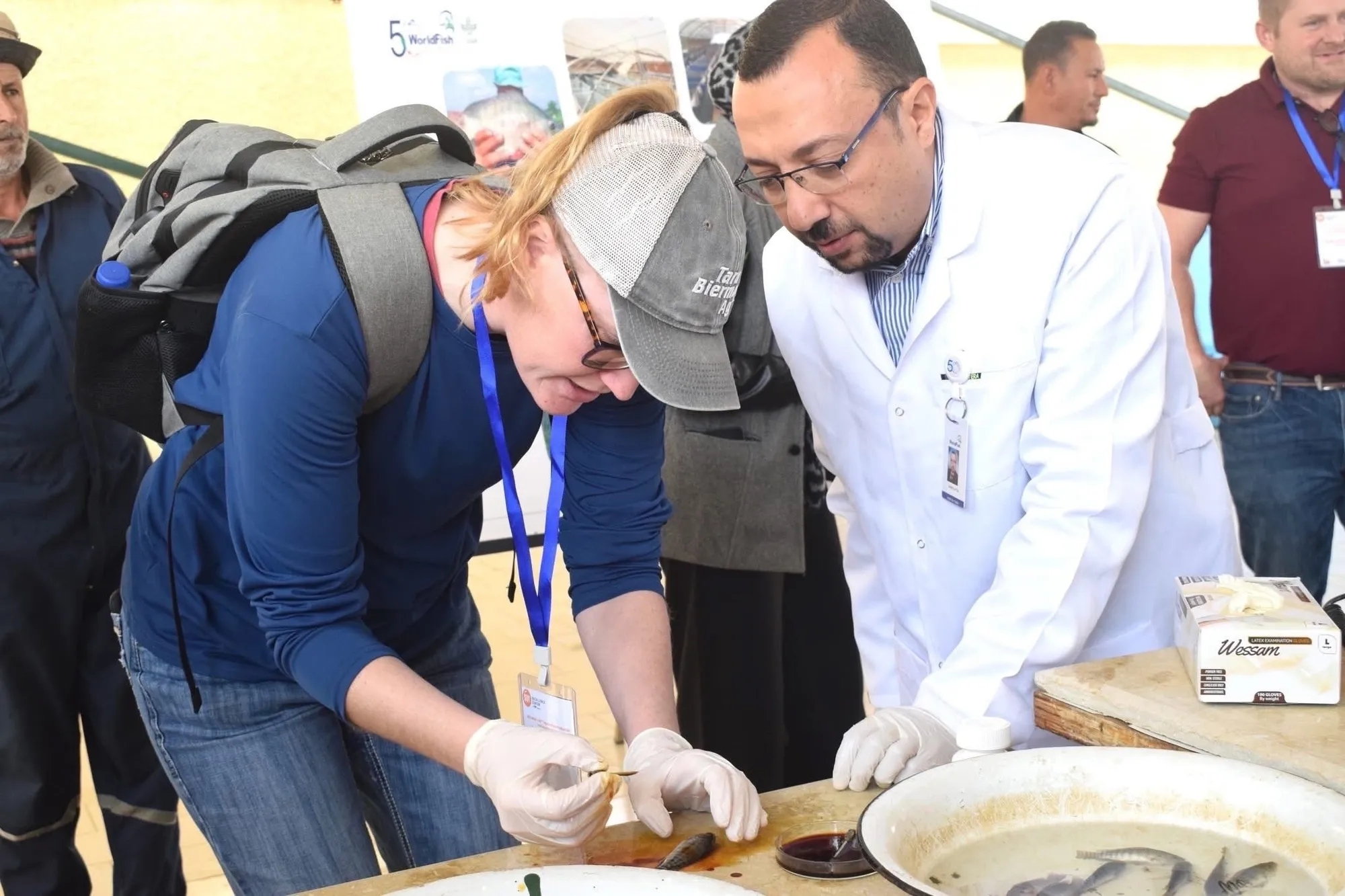 Two people wearing gloves examine a small fish specimen during a hands-on demonstration.
