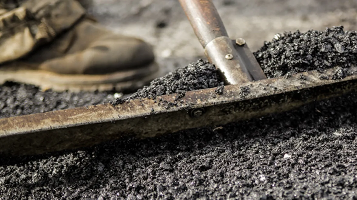 Worker applying soy-based asphalt sealant to a road surface.