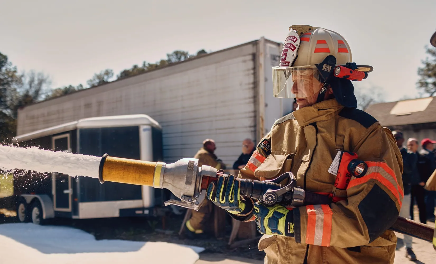 A firefighter in full protective gear sprays Firefighting SoyFoam™ from a high-pressure hose.