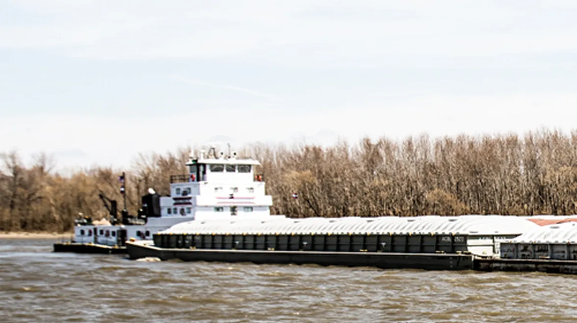 Barge loaded with soybeans traveling along a river for transport.