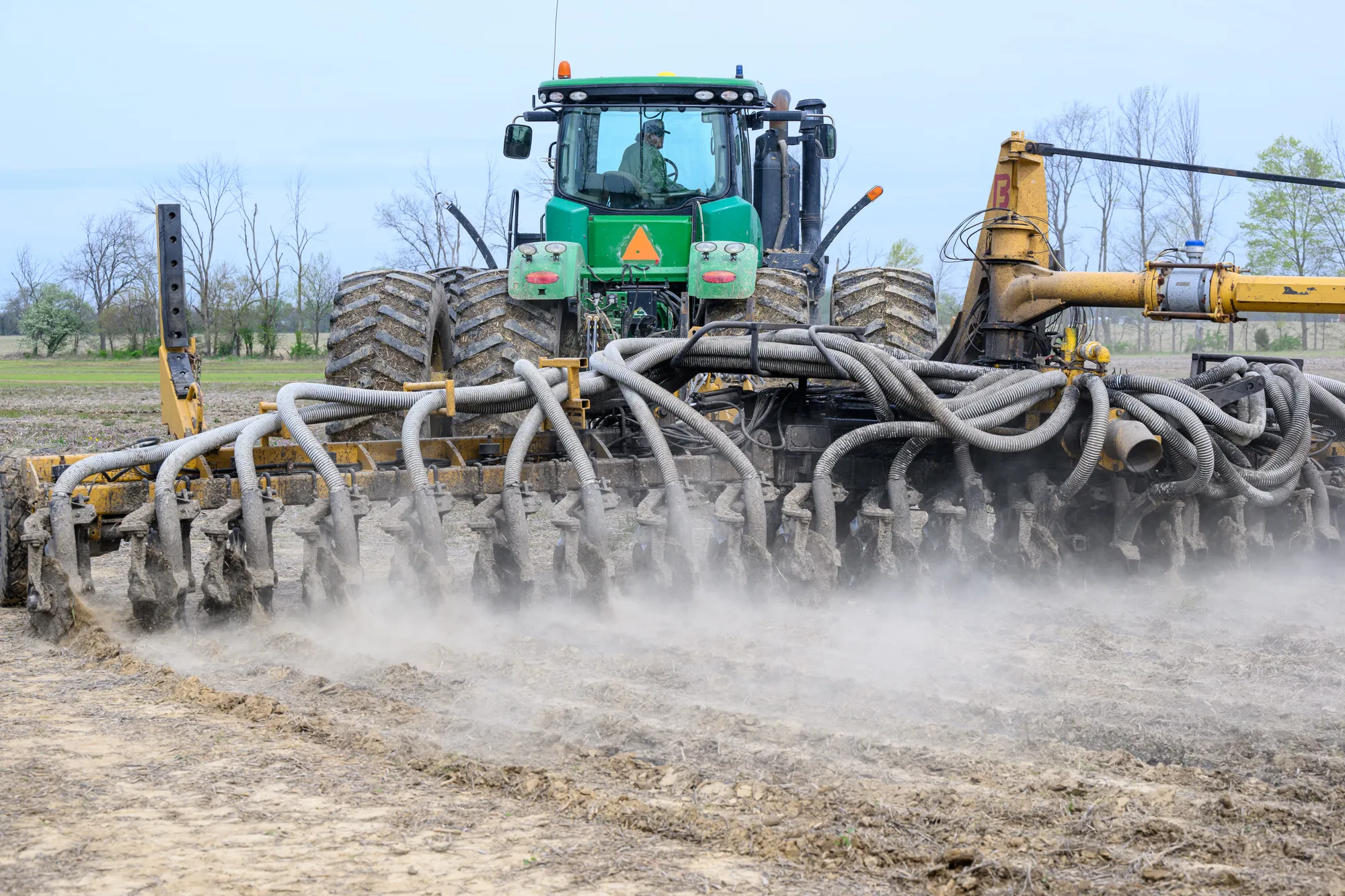 Farmer operating a tractor and nutrient applicator across a field before planting.