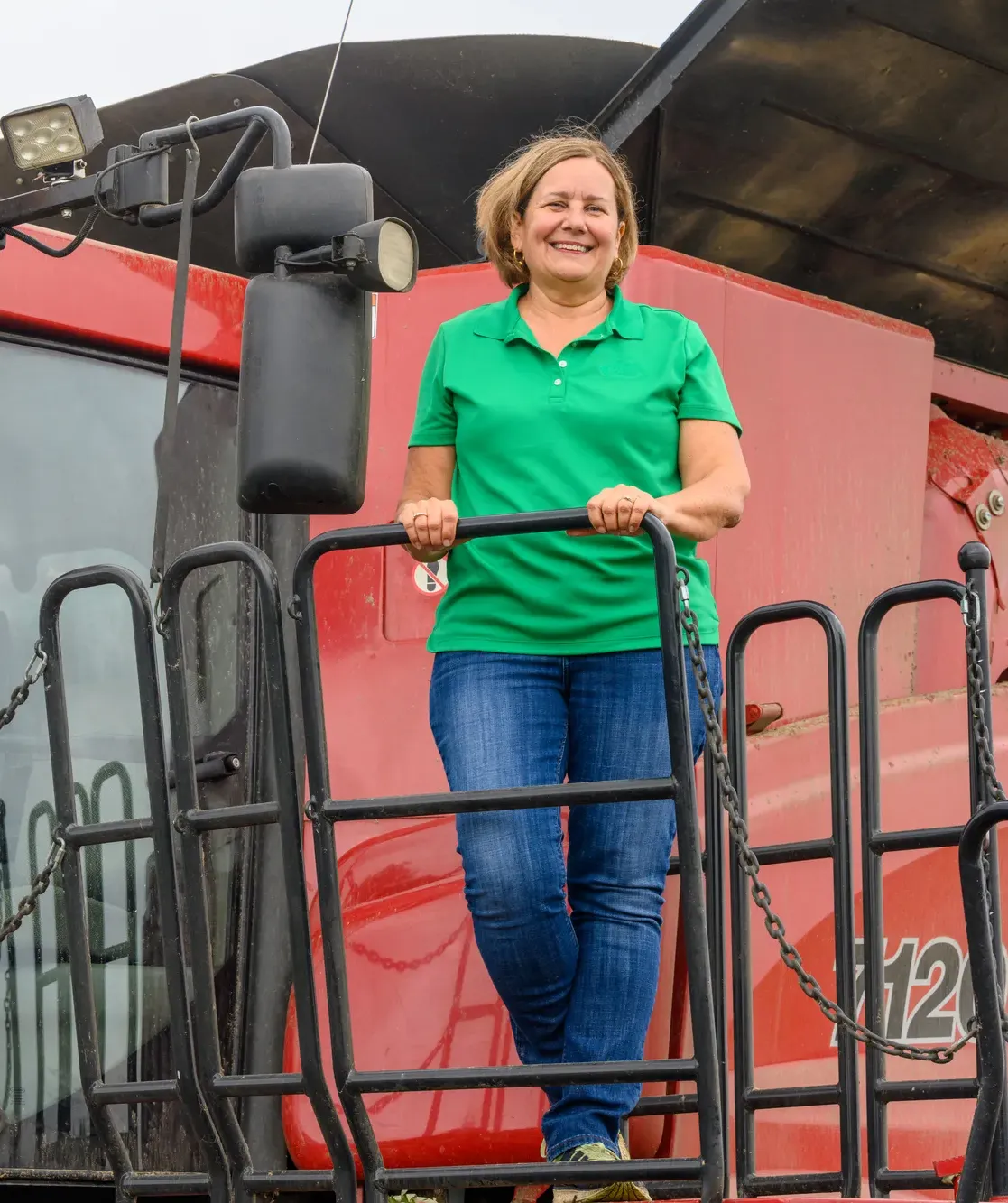 Michigan farmer standing on the platform of a combine harvester, smiling while holding the railing.