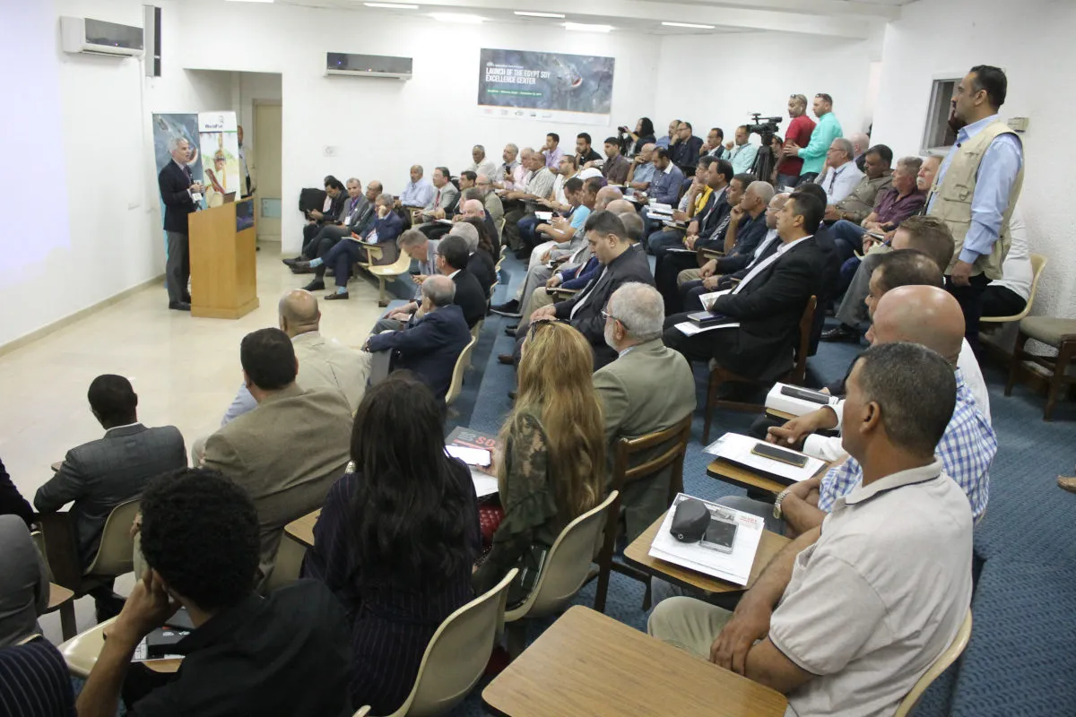 Speaker addresses a large audience seated in a conference room during an agricultural industry meeting.