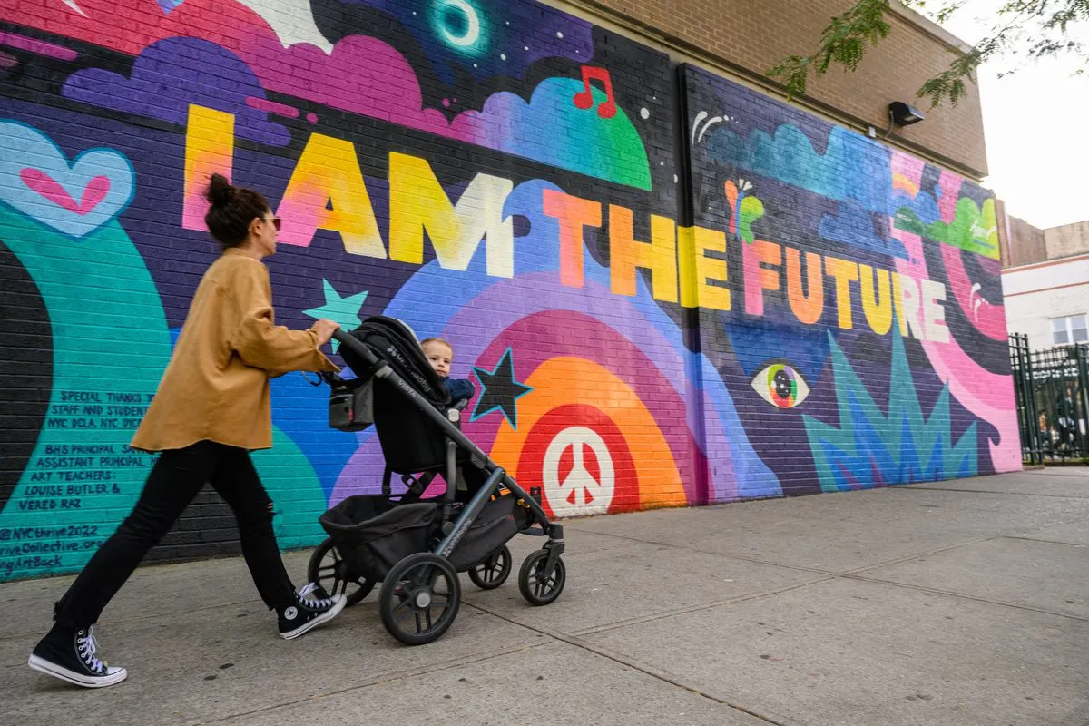 A person pushing a stroller past a colorful mural that reads ‘I AM THE FUTURE.’