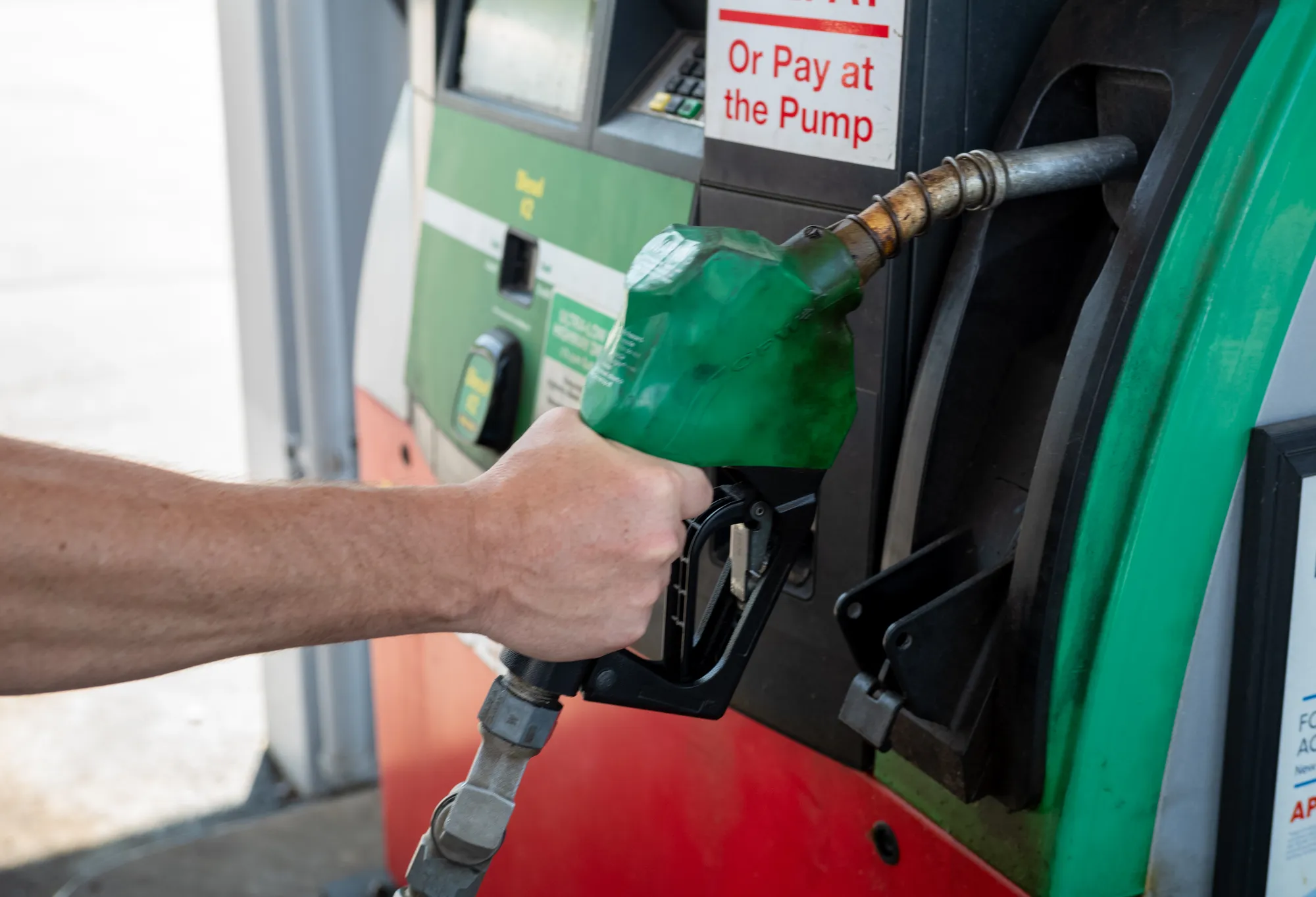 Hand removing a green biofuel nozzle from a fuel pump.