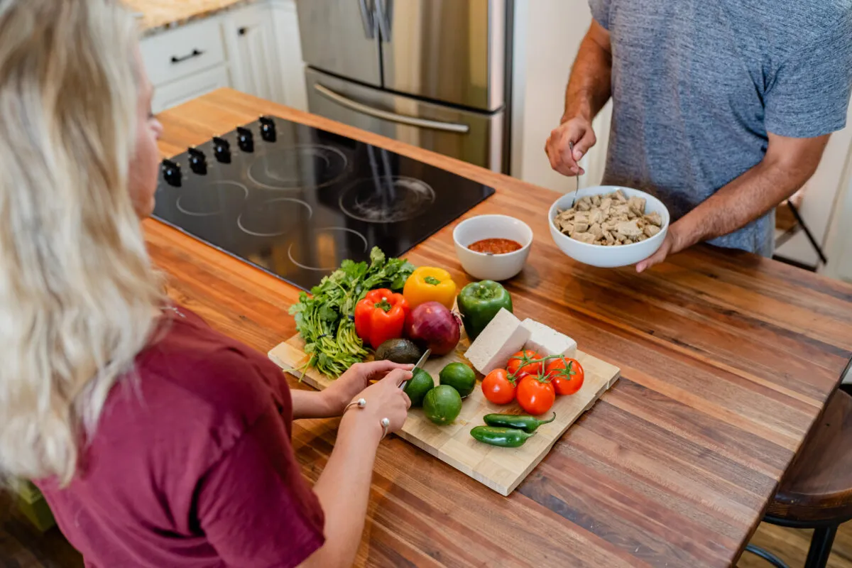 Two people preparing a meal with tofu and fresh vegetables in a kitchen.