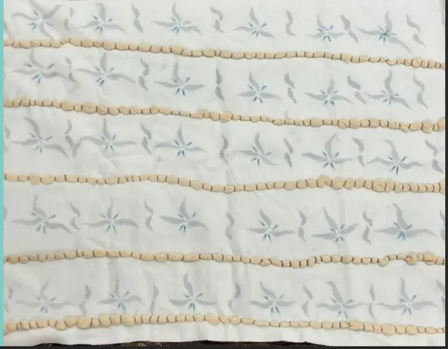 A patterned textile with a geometric floral design in soft yellow and blue tones.