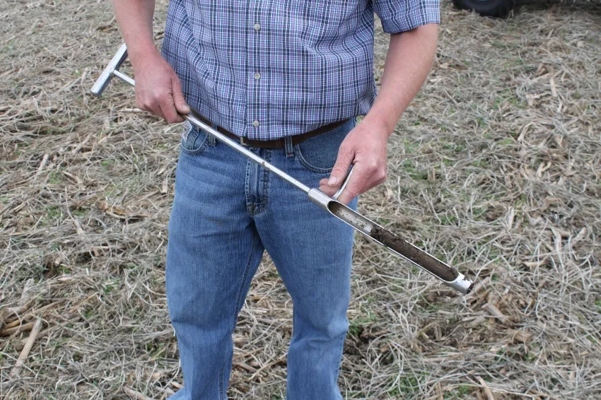 Farmer holding a soil sampling probe containing a soil sample in a crop field.