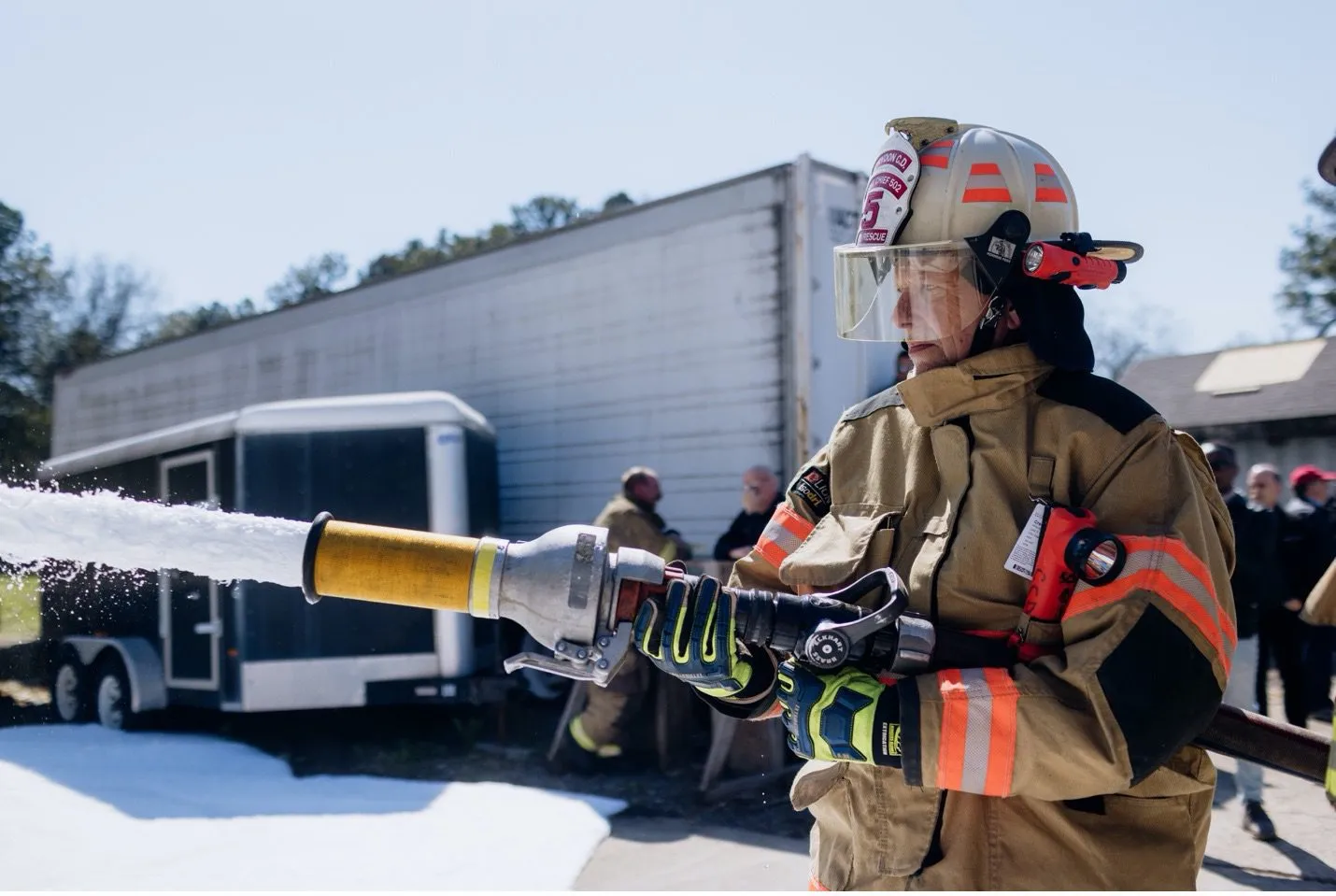 A firefighter in full gear spraying a stream of foam from a hose. 