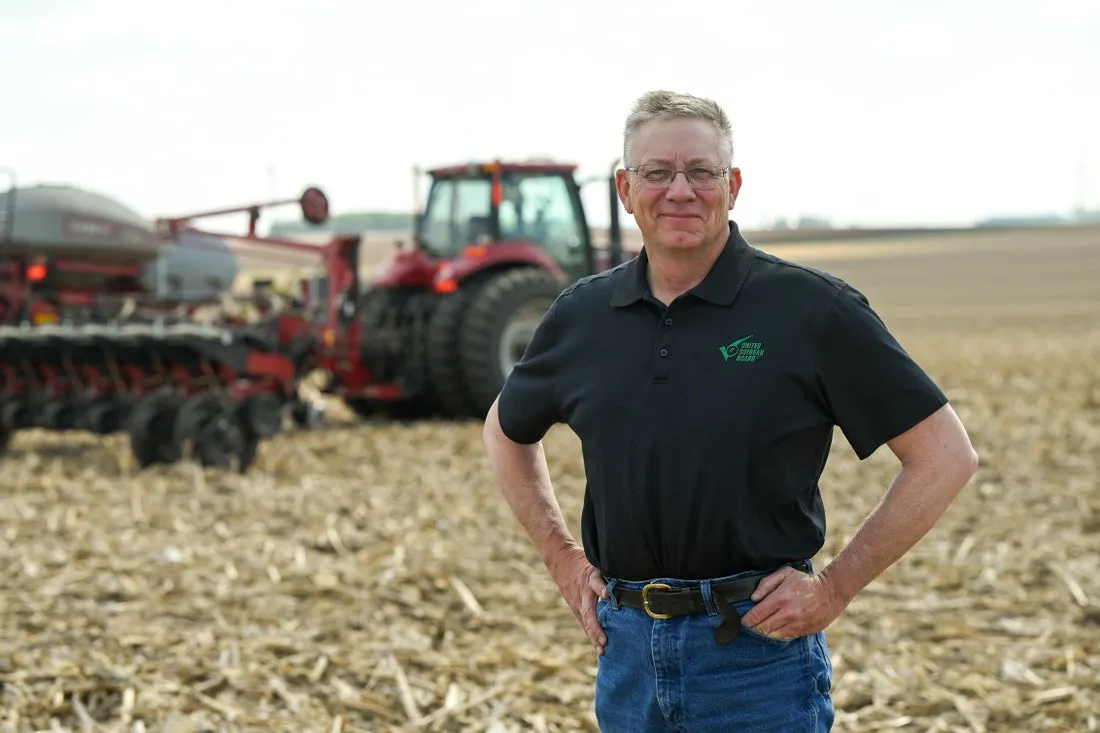 Soybean farmer and industry leader Tom Oswald stands in a field with planting equipment.
